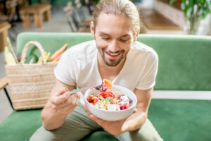 Uomo caucasico che mangia un'insalatona seduto su una panchina